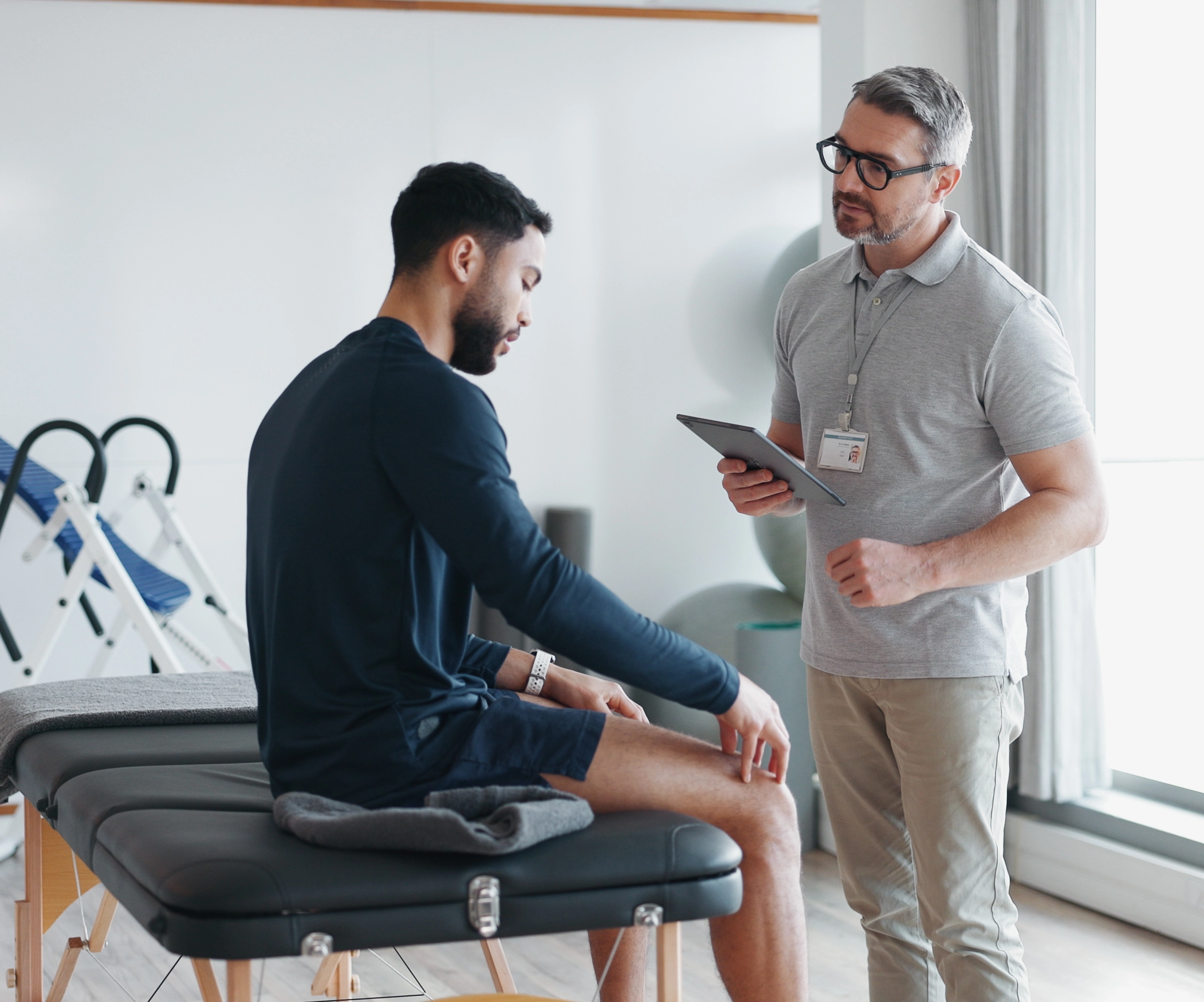 A physiotherapist reviewing knee pain with a patient using a tablet in a rehabilitation clinic.